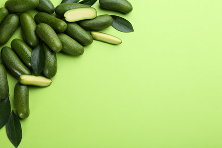 Whole and cut seedless avocados with leaves on green background, flat lay. Space for textの写真素材