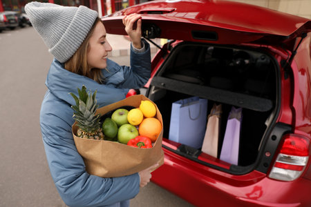 Young woman with bag of groceries near her car outdoorsの写真素材