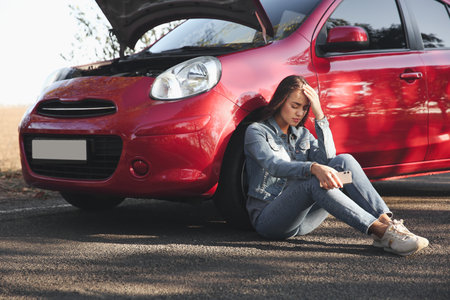 Stressed woman with smartphone near broken car outdoorsの写真素材