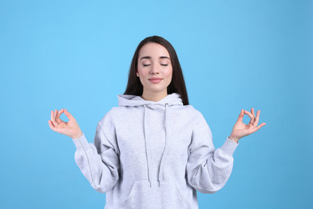 Young woman meditating on light blue background. stress relief exerciseの写真素材