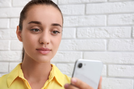 Young woman unlocking smartphone with facial scanner near white brick wall. biometric verificationの写真素材