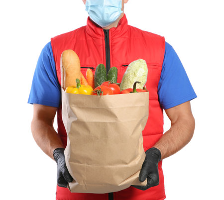 Courier in medical mask holding paper bag with food on white background, closeup. Delivery service during quarantine due to Covid-19 outbreakの写真素材