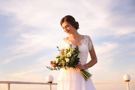 Gorgeous bride in beautiful wedding dress with bouquet near riverの写真素材