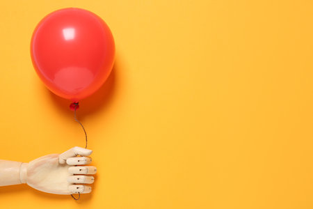 Wooden mannequin hand with red balloon on yellow background, space for textの写真素材