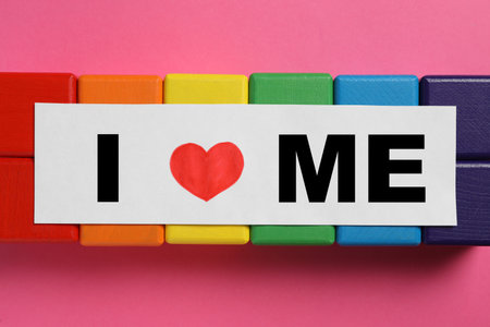 Sheet of paper with phrase I Love Me and colorful cubes on pink background, flat layの写真素材