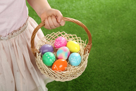 Little girl with basket full of Easter eggs on green grass, closeup. Space for textの写真素材
