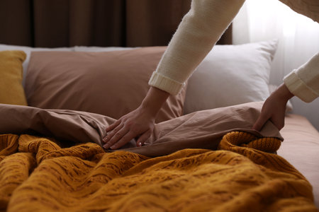 Woman making bed with brown linens, closeupの写真素材