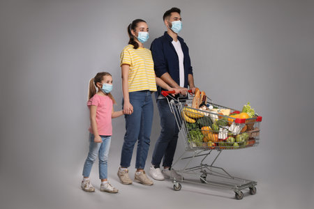 Family with protective masks and shopping cart full of groceries on light gray backgroundの写真素材