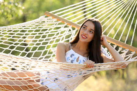Young woman resting in comfortable hammock at green gardenの写真素材
