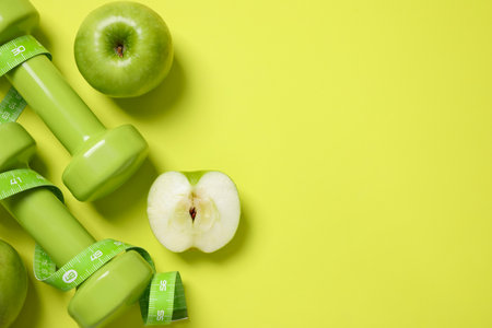 Fresh apples, measuring tape and dumbbells on green background, flat lay. Space for textの写真素材