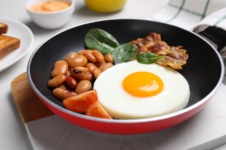 Tasty breakfast with cooked egg, beans and bacon on frying pan, closeupの写真素材