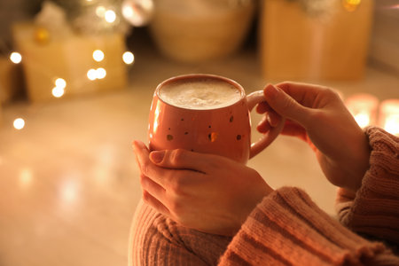 Woman with cup of drink and blurred Christmas lights on background, closeupの写真素材