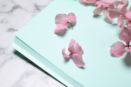 Open notebook and beautiful flowers on white marble table, closeupの写真素材