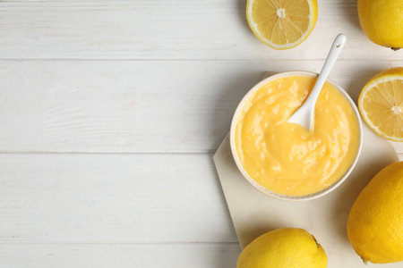 Delicious lemon curd in bowl on white wooden table, flat lay. Space for textの写真素材