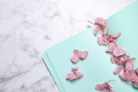 Open notebook and beautiful flowers on white marble table, flat lay. Space for textの写真素材