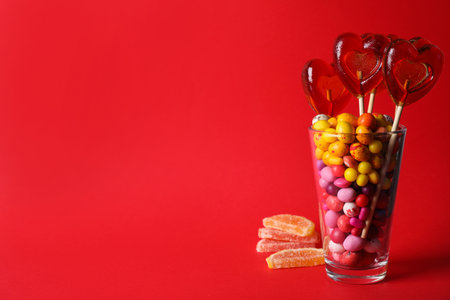 Glass with different candies on red background, space for textの写真素材
