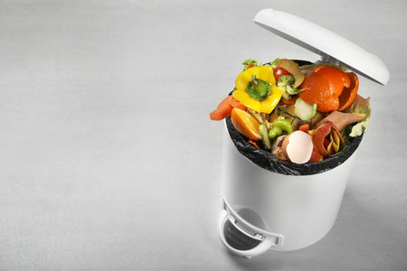 Trash bin with natural garbage on light background, space for text. Composting of organic wasteの写真素材