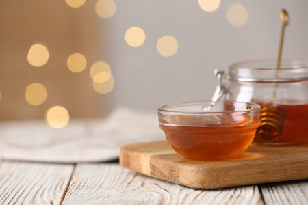 Delicious honey in glass dishware on white wooden table against blurred lights, closeup. Space for textの写真素材