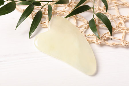 Jade gua sha tool and branches on white wooden table, closeupの写真素材