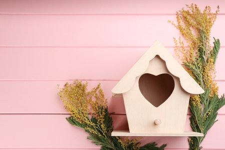 Beautiful bird house with heart shaped hole and mimosa flowers on pink wooden background, space for text. spring flat lay compositionの写真素材