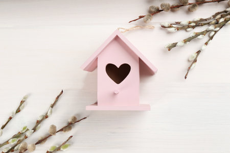 Beautiful bird house with heart shaped hole and willow branches on white wooden background. spring...