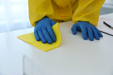Employee in protective suit and gloves sanitizing table indoors, closeup. medical disinfectionの写真素材