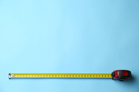 Tape measure on light blue background, top view. Space for text