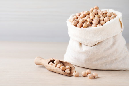 Sack and scoop with chickpeas on wooden table, space for textの写真素材