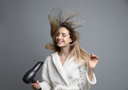 Beautiful young woman using hair dryer on gray backgroundの写真素材
