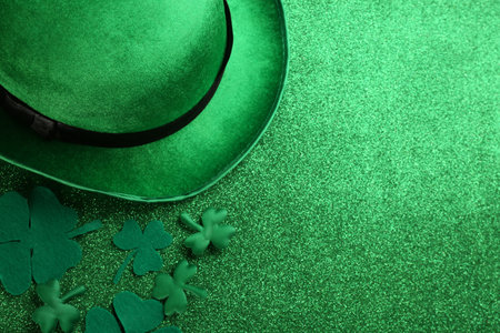 Leprechaun hat and decorative clover leaves on green glitter background, flat lay with space for text. St Patrick's Day celebrationの写真素材