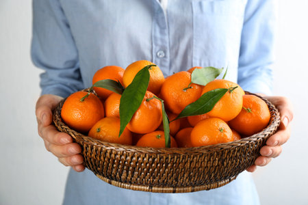 Woman holding wicker bowl with fresh tangerines on light background, closeupの写真素材
