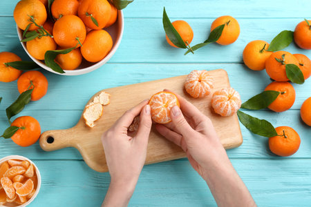 Woman peeling fresh ripe tangerine at light blue wooden table, top viewの写真素材