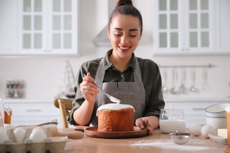 Young woman decorating traditional Easter cake with glaze in kitchenの写真素材
