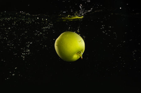 green apple falling down into clear water against black backgroundの写真素材