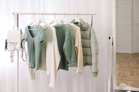 Rack with stylish warm clothes near mirror in dressing roomの写真素材