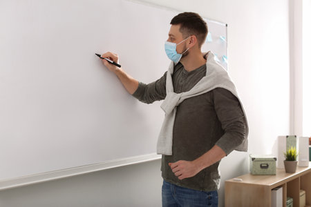 Teacher with protective mask writing on board in classroom. Reopening after Covid-19 quarantineの写真素材