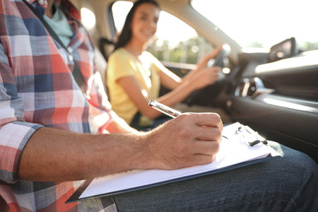 Instructor with clipboard writing result of exam in car, closeup. driving school