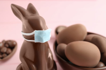 Chocolate bunny with protective mask and eggs on pink background, closeup. Easter holiday during COVID-19 quarantineの写真素材
