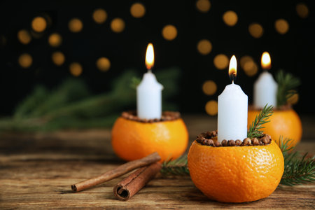 Burning candle in tangerine peel as holder on wooden table against black background, space for textの写真素材