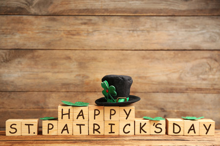Leprechaun hat, clover leaves and wooden cubes with words Happy St Patrick's Day on table, space for textの写真素材