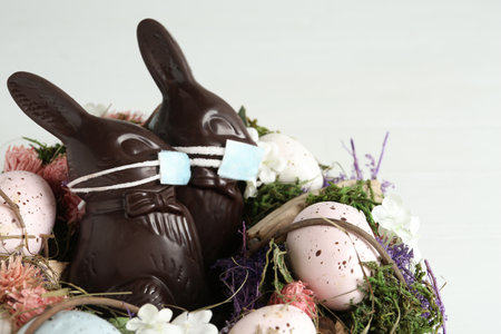 Chocolate bunnies with protective masks, eggs and wreath on white background, closeup. Easter holiday during COVID-19 quarantineの写真素材