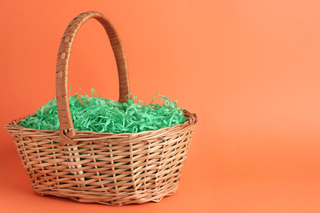 Easter basket with green paper filler on coral background, space for textの写真素材