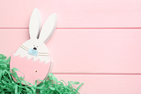 Cute bunny figure in protective mask on pink wooden background, top view with space for text. Easter...