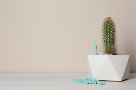 Beautiful house plant and fertilizer sticks on white wooden table against beige background. Space for textの写真素材