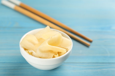 Spicy pickled ginger and chopsticks on light blue wooden table, space for textの写真素材