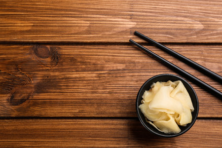 Pickled ginger in bowl and chopsticks on wooden table, flat lay. Space for textの写真素材