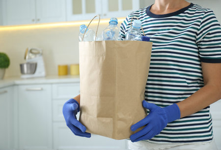 Woman holding paper bag with used plastic bottles indoors, closeup. recycling problemの写真素材
