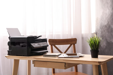 Modern printer, tablet and office supplies on wooden table indoors