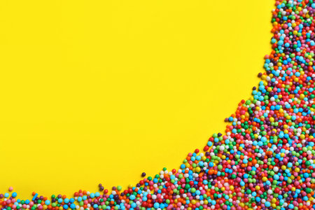 Bright colorful sprinkles on yellow background, flat lay with space for text. Confectionery decorの写真素材