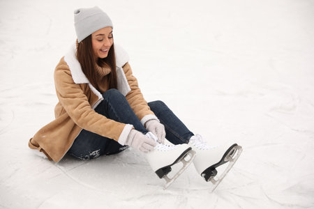 Woman lacing figure skate while sitting on ice rinkの写真素材